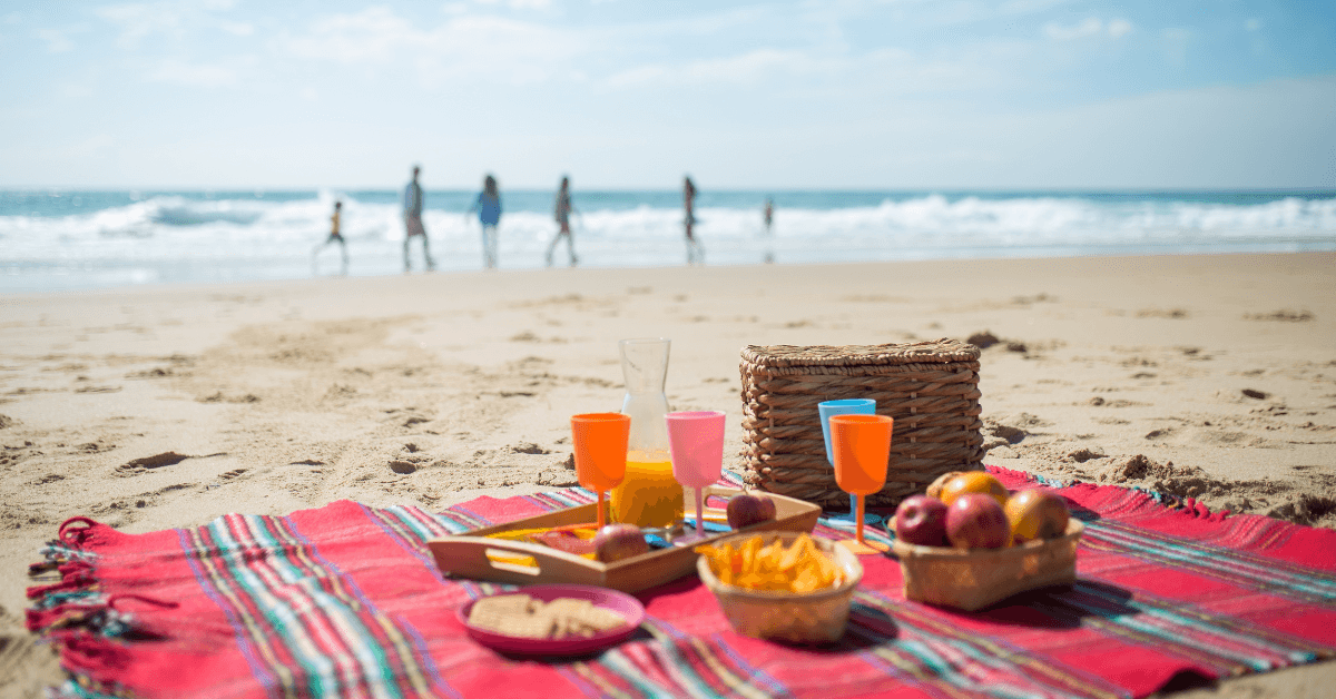 Beach picnic setup with fruit, drinks and a basket on a sandy Hermanus Beach 